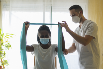 A medical professional helping a woman hold a piece of fabric between her hands, with her arms raised over her head