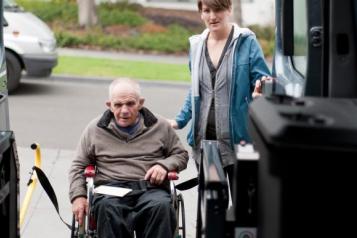 Man in a wheelchair being helped into a bus