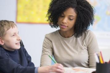 In a classroom, a woman helps a young boy in a wheelchair