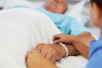 man lying down in a hospital bed with a child holding his hand
