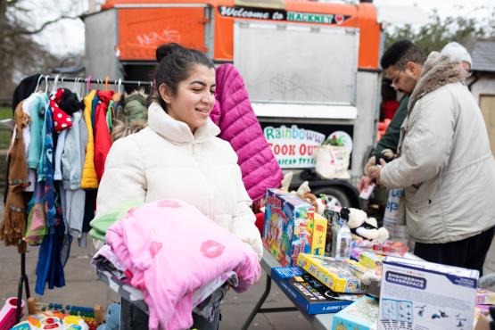 A woman at a stall in a market, carrying a pink blanket.