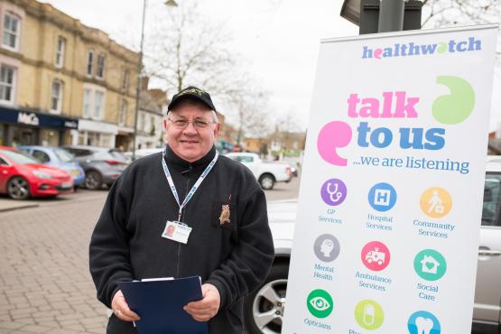 A man standing outside, in front of a multicoloured Healthwatch banner