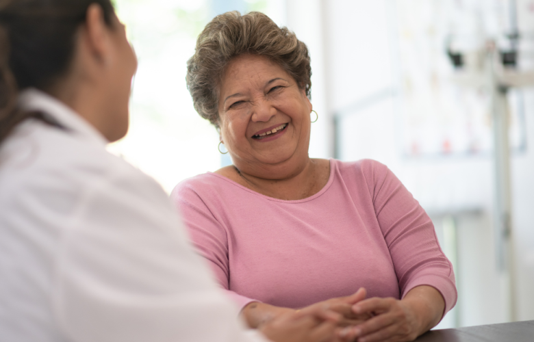 A woman speaking to a doctor. She is smiling and wearing a pink jumper.