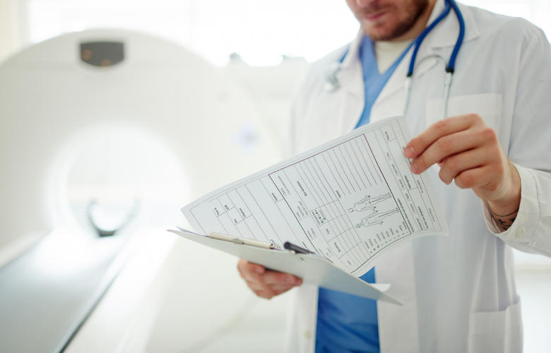 A doctor looking at some paperwork, standing in front of a CT scanner