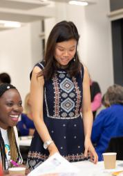 A diverse group of women sitting around a table, laughing and talking to each other.