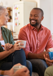 Four adults sitting in a living room, smiling, chatting, and drinking from mugs