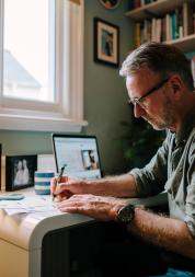 A man sitting at a desk with a laptop, taking notes