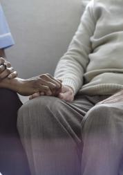 A nurse holding an old man's hand on the sofa.